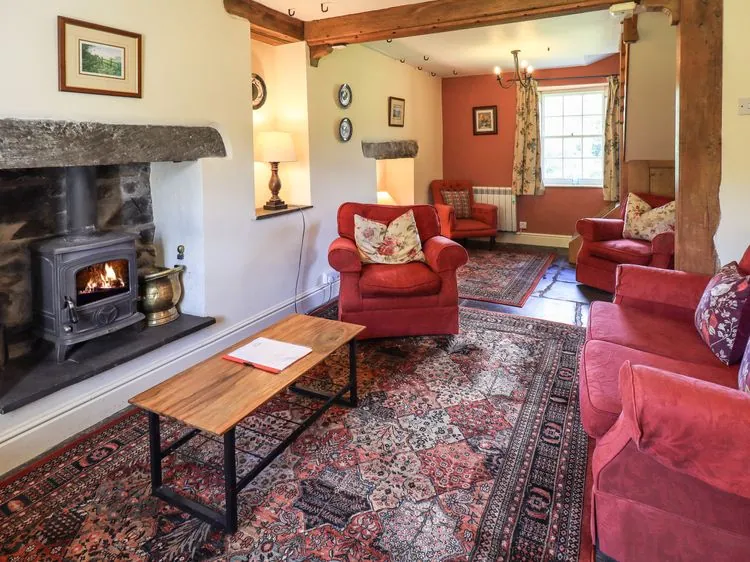 A living room with red armchairs wooden coffee table and a fireplace at Ellis Howe in Torver