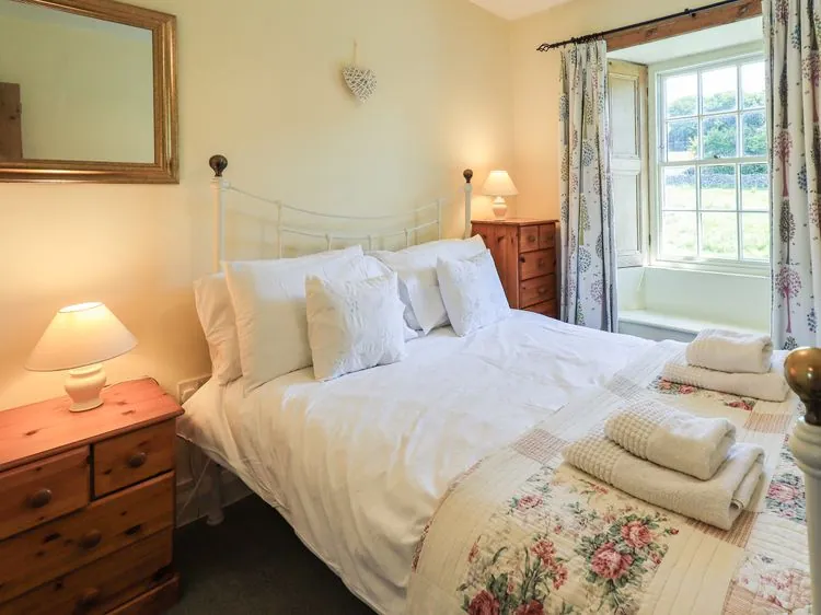A bedroom with a double bed with white bedding and floral quilt with bedside tables and lamps at Ellis Howe in Torver